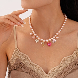 Détail du collier de perles roses avec cœur en strass, nœud doré et pendentif Hug Me