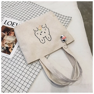 Detail of corduroy tote bag with rabbit embroidery and cow pendant on plaid backdrop