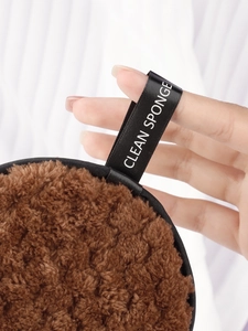 Close-up of brown round cleansing puff with black satin strap and soft plush texture