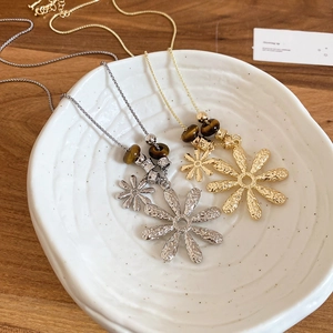 Detail of tiger eye stone bead and textured daisy flower pendant in a ceramic bowl