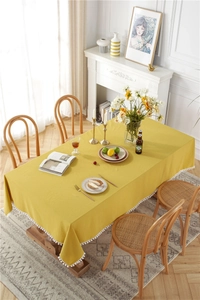 Detail of yellow cotton tablecloth featuring white pom pom fringe and soft texture