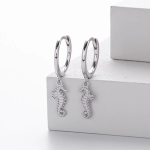 Detailed view of silver seahorse hoop earrings hanging on a white geometric block