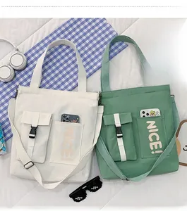 Detail of canvas tote bags with 'NICE!' lettering, dual front pockets and adjustable strap