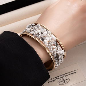 Close-up of a wide gold open bangle featuring white and grey crushed stone inlays