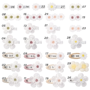 Flat lay of 29 different styles of embroidered floral hair clips for kids on a white surface