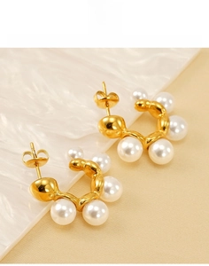 Macro view of C-shaped gold-plated pearl stud earrings with gradient size arrangement