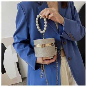 Detail of champagne rhinestone cylinder bag with large pearl handle and metal chain