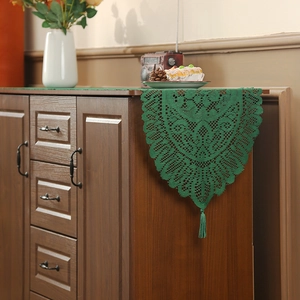 Green knitted table runner with tassels on a wooden cabinet in a warm home setting