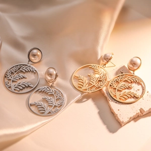 Elegant gold and silver leaf drop earrings with pearl studs on a textured stone