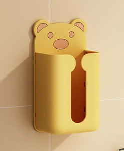 Detail of a wall-mounted yellow bear tissue box on a beige tiled bathroom wall