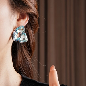 Macro shot of a geometric floral stud earring with blue and amber crystals on a model