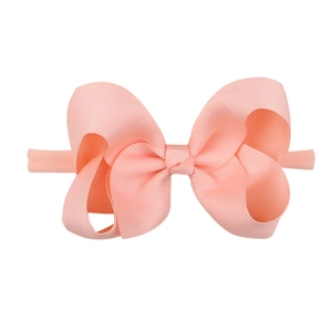 Detail showing a soft pink grosgrain bow headband for babies on a clean white backdrop