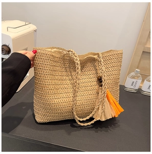 Detail shot of a beige straw tote bag with a decorative orange and beige fringe tassel