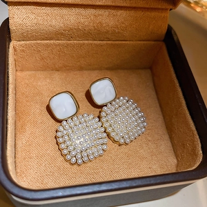 Detailed macro view of square enamel earrings with gold edges and faux pearl inlay