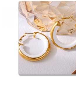 Detail view of gold hoop earrings with white enamel finish on a textured surface