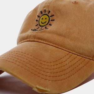 Close-up of yellow cotton baseball cap featuring embroidered sun smiley and distressed brim