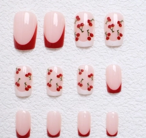 Close-up of red French tip press-on nails with sweet cherry pattern on white surface