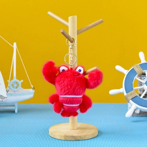 Detailed view of a cute red plush crab keychain hanging on a wooden jewelry stand