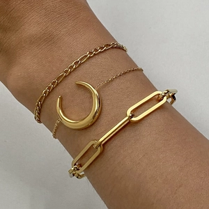 Detail showing stacked golden Figaro, moon pendant, and paperclip style chain bracelets