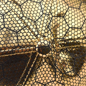 Macro shot of gold honeycomb pattern on cotton cap with metallic texture and black stitching