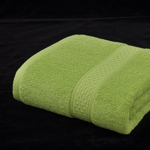 Asciugamano in cotone verde erba piegato con trama in spugna e bordi decorati