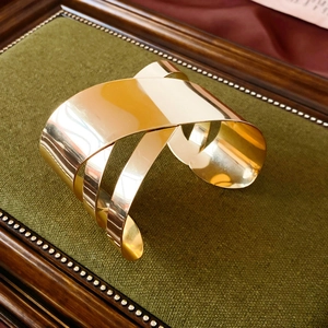 Polished gold-plated wide crossover cuff bracelet with a modern multi-layer design