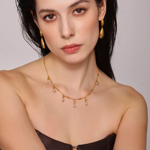 Detail of gold necklace and bird earrings set with freshwater pearls on a model