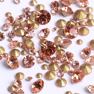 Macro shot of loose sparkling peach rhinestones and bronze cone base nail gems