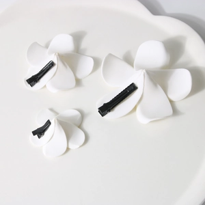 Three sizes of white plumeria flower hair clips on a cloud tray for beach styling