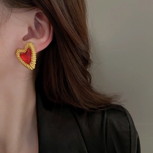 Detaillierte Nahaufnahme des golden gerahmten roten Herz-Ohrrings am Ohr des Models.