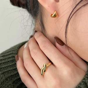 Close-up of elegant gold geometric earrings and a twisted ring worn by a model