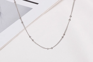 Detail of silver stainless steel curb chain with bead accents lying on white surface
