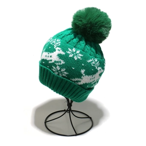 Detail of green knit beanie with white reindeer snowflake patterns and large pom-pom