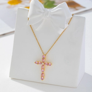 Detailed view of gold cross pendant with pink pear-cut zircon on white display stand