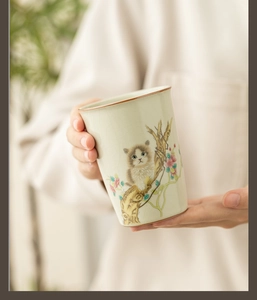 Close-up of hands holding Ru ware ceramic tea cup with cute cat and flower crackle glaze