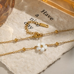Minimalist 18K gold plated necklace with a white shell flower pendant on textured paper