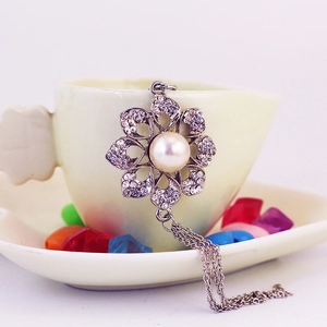 Silver flower keychain with white pearl and crystal tassels hanging on a beige cup