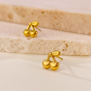 Close-up of polished gold cherry stud earrings showcasing metallic leaf and fruit details