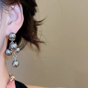 Detail of silver drop earrings featuring clustered grey pearls on a model's ear