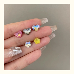 Macro detail of sparkling crystal heart and star nail charms held for scale