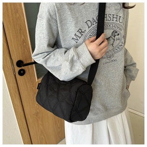 Détail d'un sac bandoulière cylindrique noir matelassé montrant la texture et les coutures