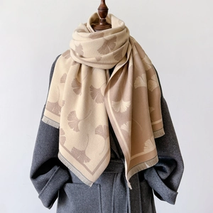 Detail of beige scarf with ginkgo leaf patterns and soft tassels on a grey wool coat