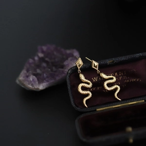 Macro detail of snake drop earrings with scale texture on vintage purple velvet box