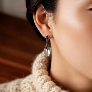Close-up of a silver spoon-shaped earring with a polished metallic finish on a model