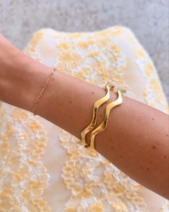 Close-up of golden wave cuff bracelets and delicate chain bangles worn by a model