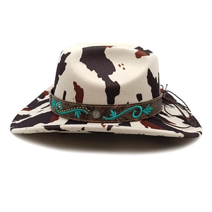 Detail of cow print cowboy hat featuring brown leather band with turquoise embroidery