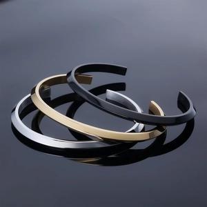 Minimalist C-shaped open bangles in gold silver and black finishes on a grey surface