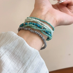 Detail of bohemian layered bead bracelets in blue and green tones worn on wrist