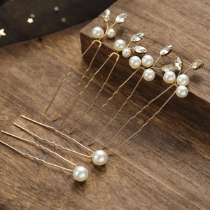Five gold bridal hair pins with pearls and crystal leaves set on a dark wood background