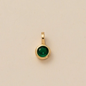 Close-up of gold pendant featuring a round-cut emerald green zircon on textured paper